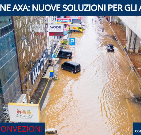 Strada allagata con veicoli che attraversano l'acqua, affiancata da un edificio commerciale e da un ponte sopraelevato.