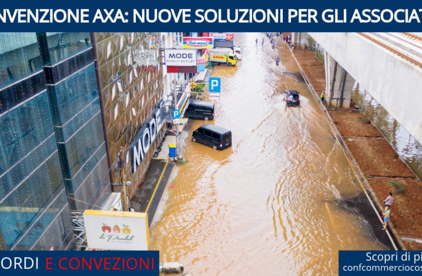 Strada allagata con veicoli che attraversano l'acqua, affiancata da un edificio commerciale e da un ponte sopraelevato.