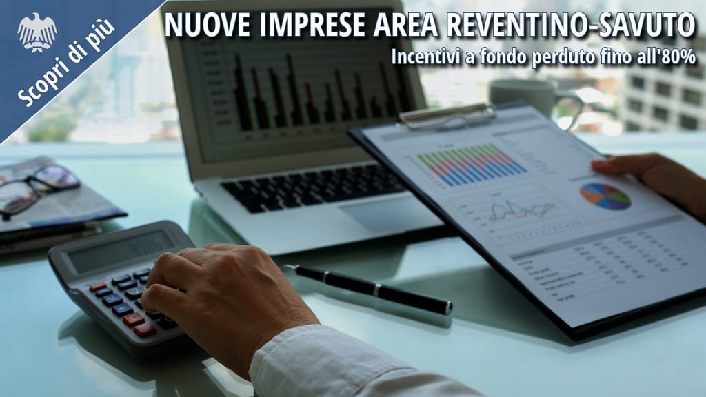 Imprenditore analizza dati economici su laptop e documenti per avvio nuova impresa con incentivi in Calabria.